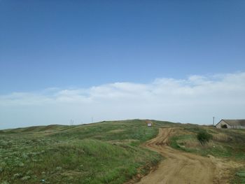 Dirt road amidst grassy landscape against blue sky