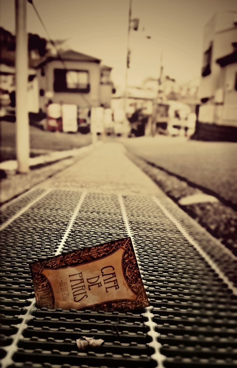 focus on foreground, text, communication, street, transportation, the way forward, guidance, western script, close-up, building exterior, road, built structure, selective focus, surface level, city, diminishing perspective, sky, architecture, outdoors, no people