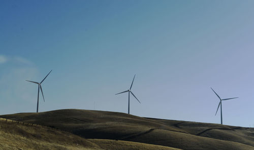 Low angle view of wind turbines on mountain against sky