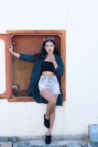 Portrait of young woman standing against wall