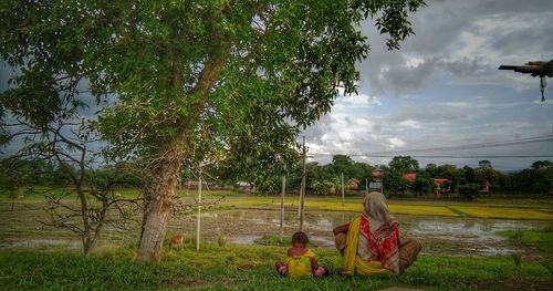 Rear view of people sitting on land against trees