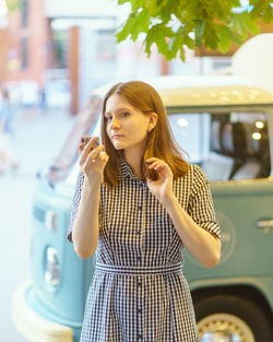 Portrait of beautiful young woman looking in mirror and correcting makeup in city, enjoying summer