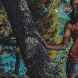 Side view of shirtless man standing by tree trunk