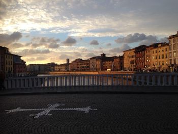 Bridge over river amidst buildings against sky during sunset