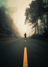 Rear view of man running on road during foggy weather