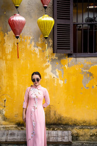 Woman with vietnam culture traditional dress standing against the yellow wall in hoi an vietnam.