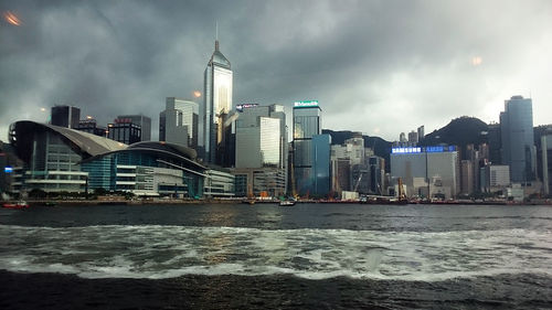 City at waterfront against cloudy sky