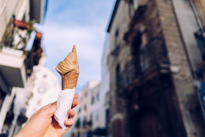 Close-up of hand holding ice cream against sky