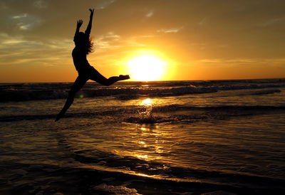 Silhouette woman jumping on shore at beach against sky during sunset