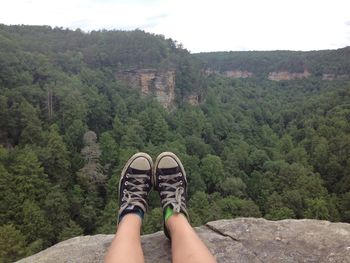 Low section of person wearing canvas shoes on cliff against forest