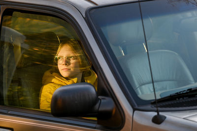 Boy sitting in car looking out passanger window tword setting sun