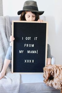 Girl holding board with text while sitting on sofa at home