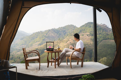 Man sitting on chair and table against mountain