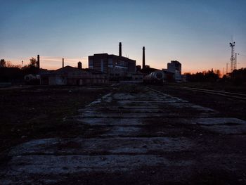 Road by silhouette buildings against sky at sunset