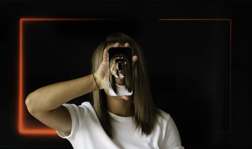 Portrait of young woman standing against black background