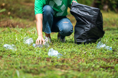 A female activist picking up garbage plastic bottles into a plastic bag in the park for recycling