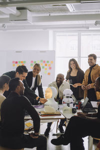 Multiracial students and professors discussing over social robot in innovation lab