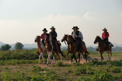 People riding horses on field against sky