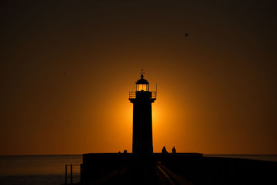 Silhouette lighthouse on beach against sky during sunset