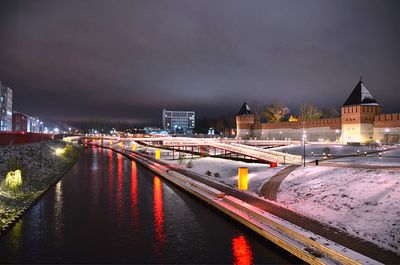 Illuminated bridge over river amidst buildings in city at night