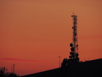 Low angle view of communications tower against orange sky