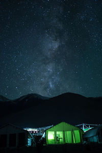 Illuminated tent by mountains against sky at night