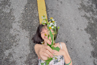 High angle view of woman holding plant lying down on road