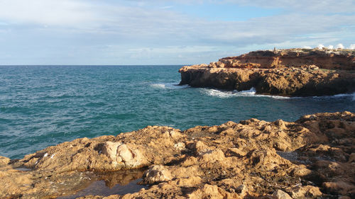 Scenic view of rocks by sea against sky