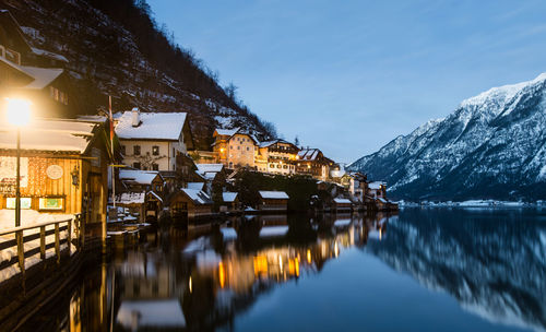 Illuminated buildings by mountains and sea against sky at dusk