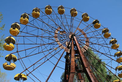 Low angle view of abandoned ferris wheel against clear blue sky