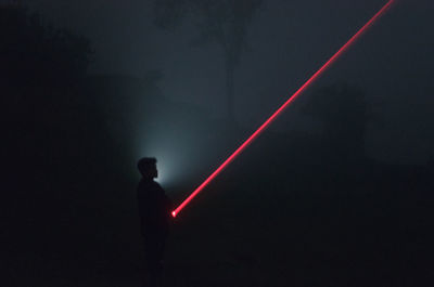 Silhouette man standing on illuminated road at night