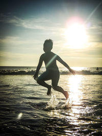 Full length of boy standing on sea against sky during sunset