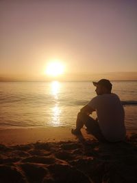 Rear view of man sitting on beach against sky