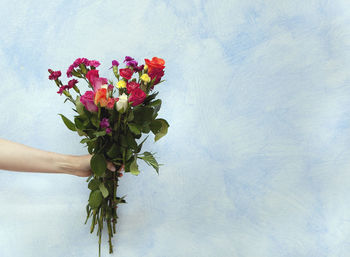 Cropped hand holding bouquet against wall