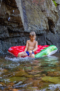 Full length of shirtless boy on rock in water