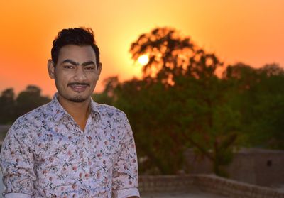 Portrait of young man standing against orange sky during sunset