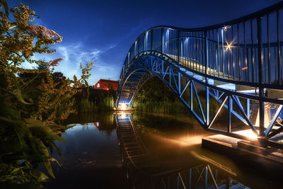 Illuminated bridge over river against sky at night