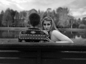 Woman sitting on bench by lake against sky