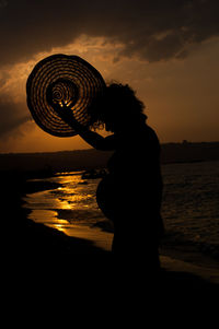 Silhouette man standing on beach against sky during sunset