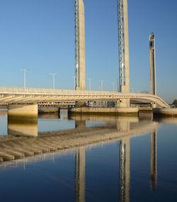 Reflection of bridge on water against clear blue sky