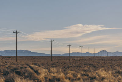 Electricity pylons on field against sky