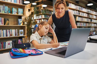 Teacher helping to solve and finish task. bored little student girl doing her homework using laptop