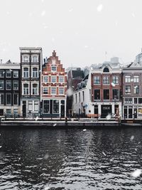 Buildings by river in city against sky during winter