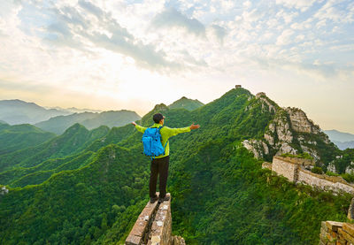 Rear view of man with arms outstretched standing on cliff at great wall of china