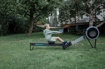 Boy using the rowing machine in his garden at home exercising