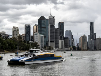 Boats in river by buildings in city against sky