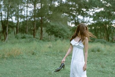 Woman holding shoes while standing on grassy field