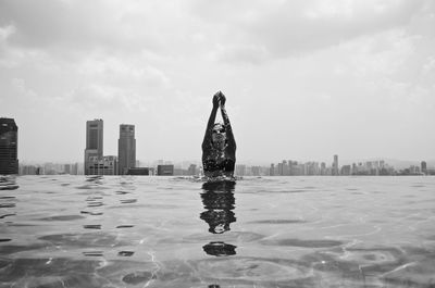 Digital composite image of person in swimming pool by buildings against sky