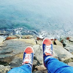 Low section of man sitting on rocks by sea