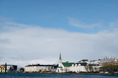 Sailboats in sea by buildings against sky